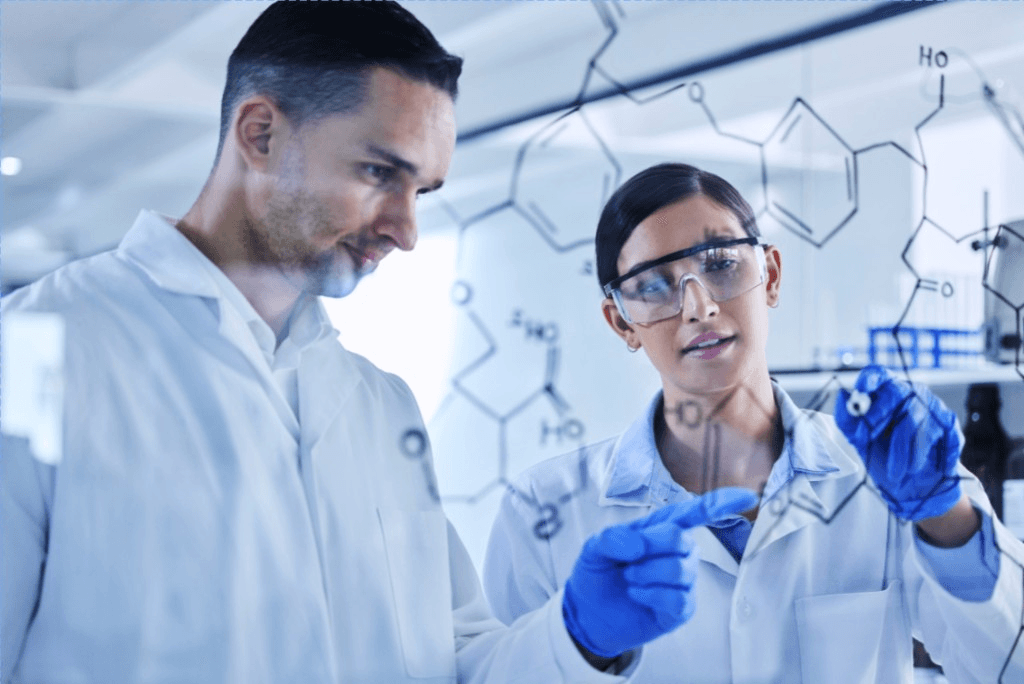 Scientists in lab coats reviewing chemical structures on a glass board