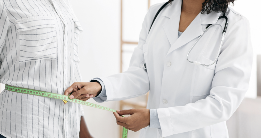 Doctor measuring a patient's waist with a tape measure in a clinical setting