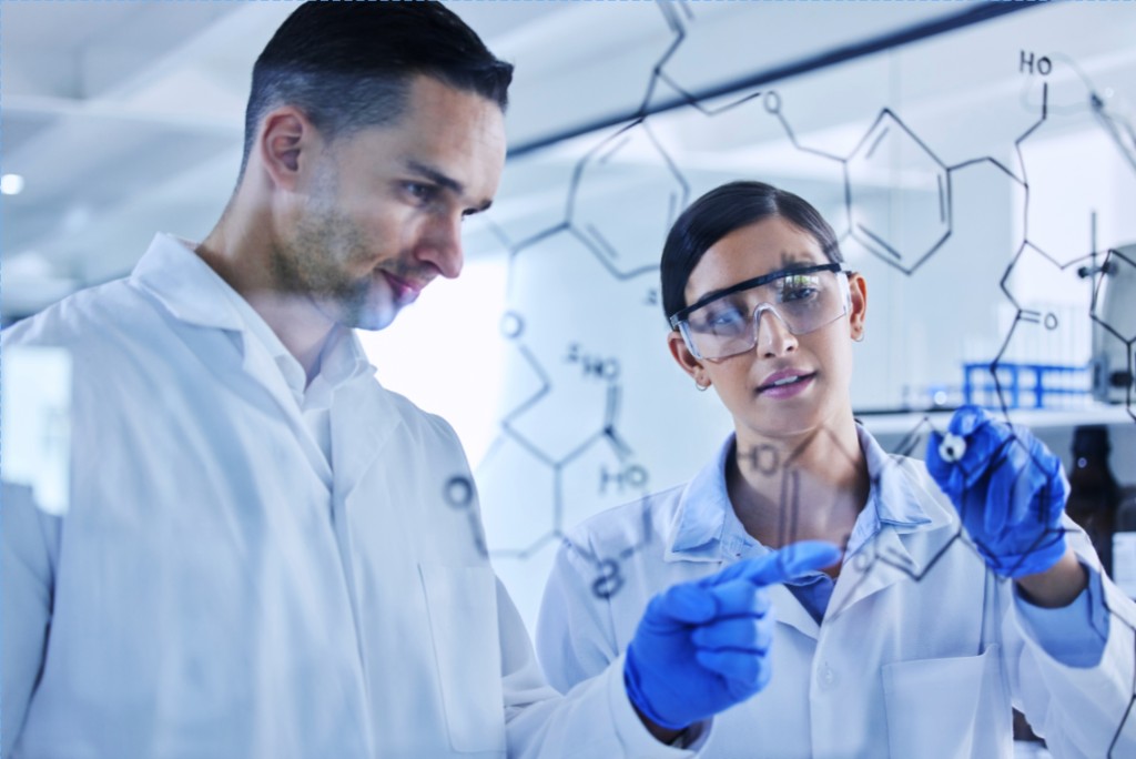 Scientists in lab coats reviewing chemical structures on a glass board